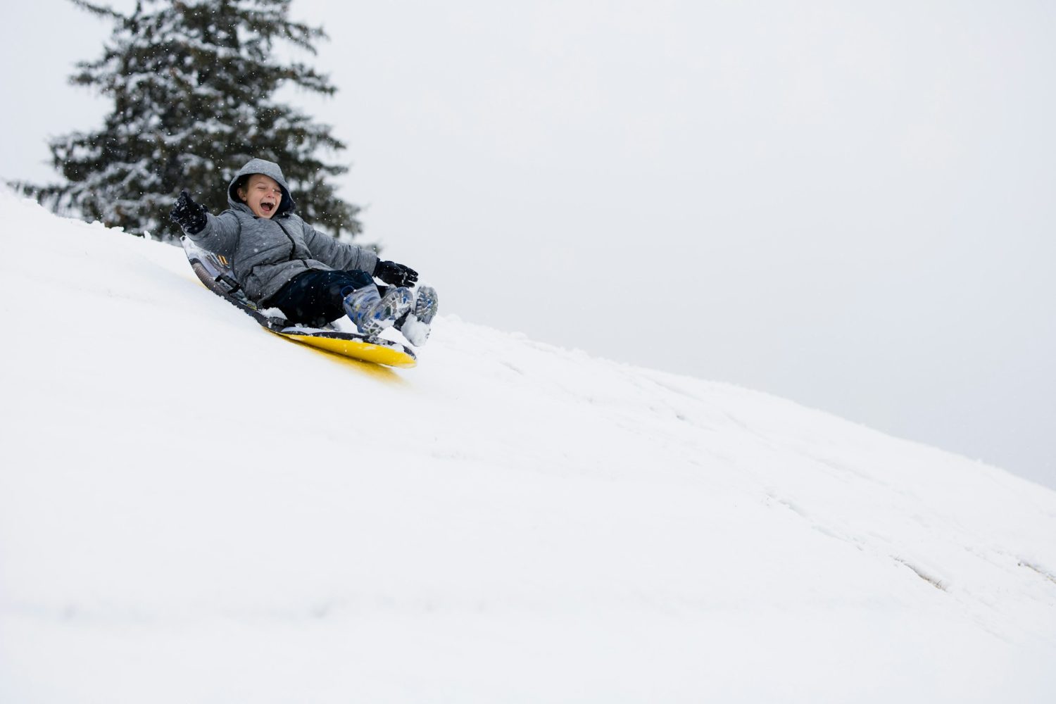 Kid sliding down snowy mountain on yellow sled. Poconos PA with kids.