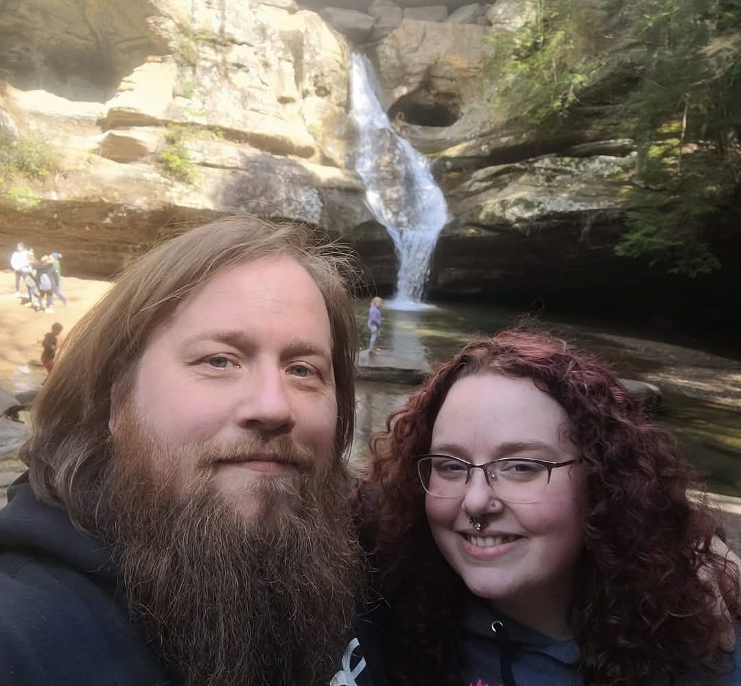Couple smiling and standing in front of Cedar Falls. Hocking Hills Romantic Getaways.