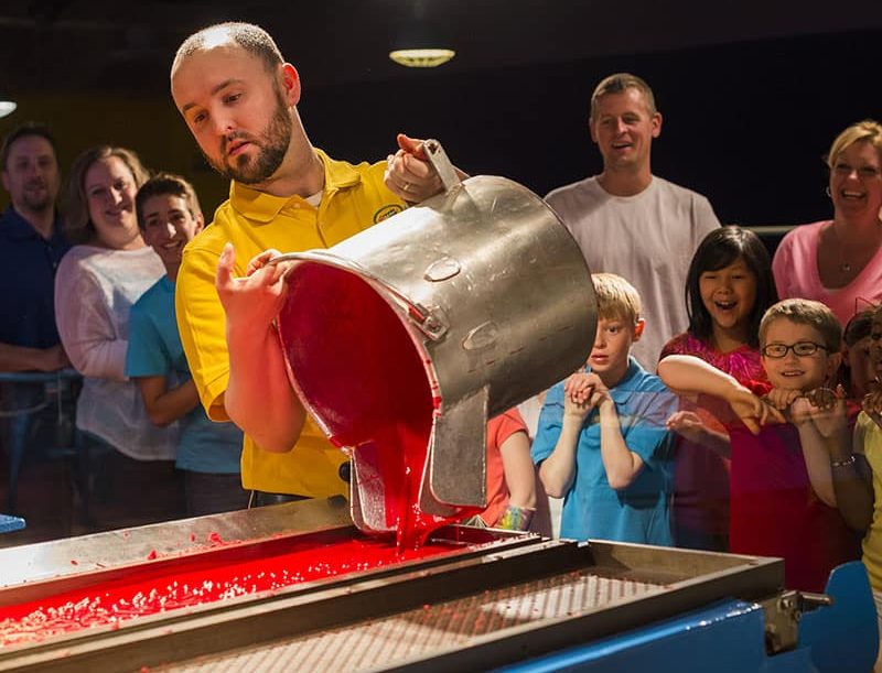 A man pouring red wax into a flat pan.