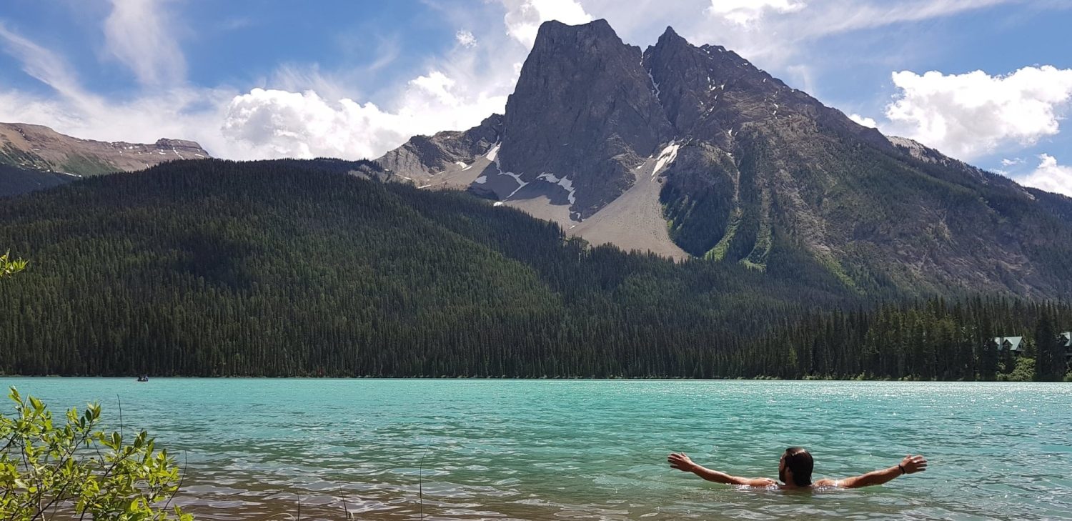 Man swimming in turquoise waters in front of a mountain range. Things to do in Glacier National Park Montana.
