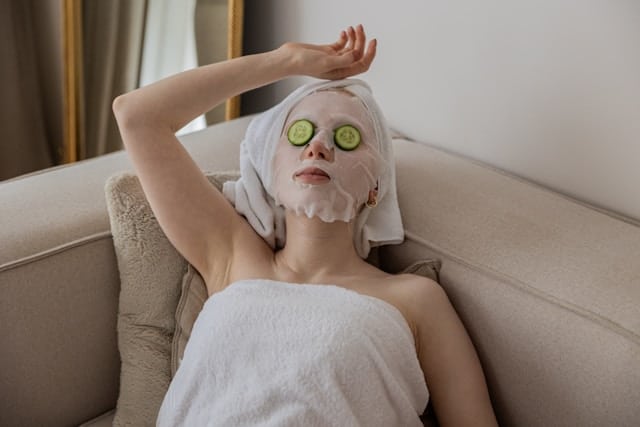 woman in towel and cucumber slices over eyes, lying down on couch