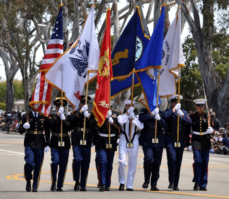 eight soldiers of all branches of US military standing in a line facing camera holding branch flags