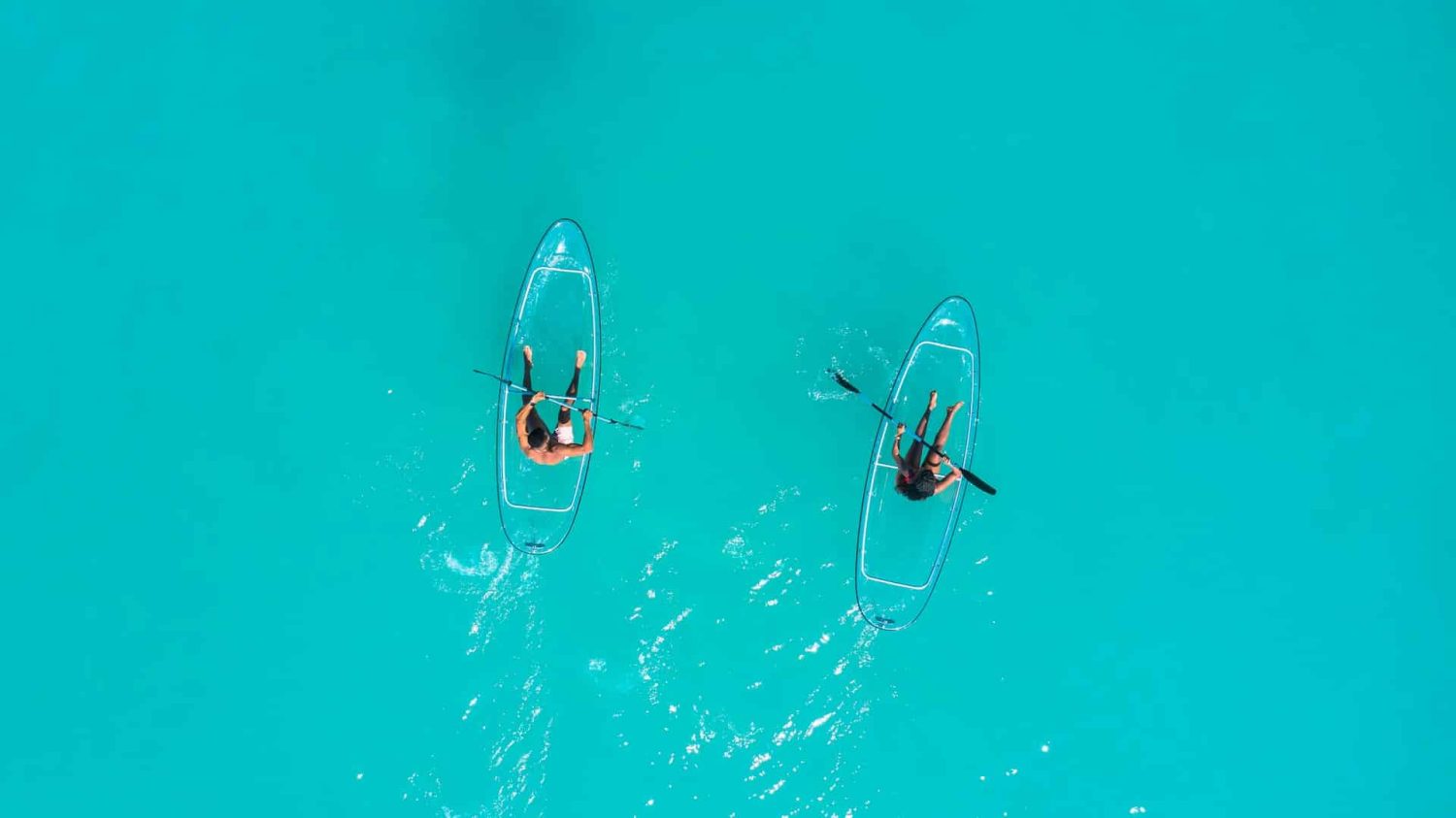 Two people on clear kayaks in turquoise waters. Best beaches in Antigua. 
