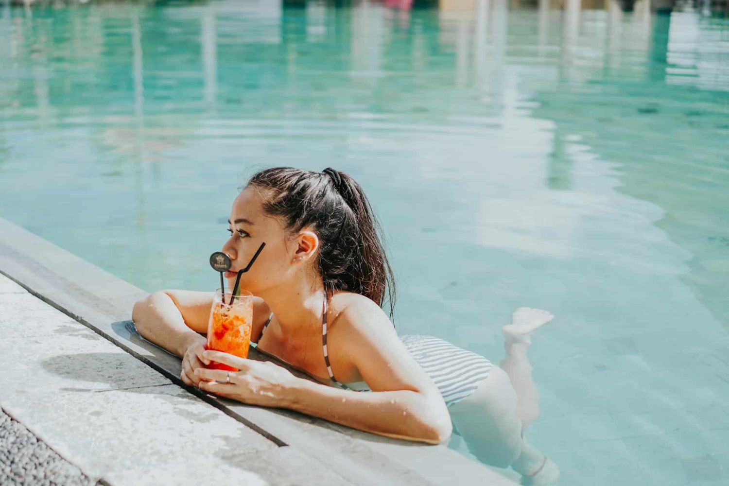 Woman in bathing suit on side of pool with cocktail in hand. Baby-friendly Caribbean resorts.