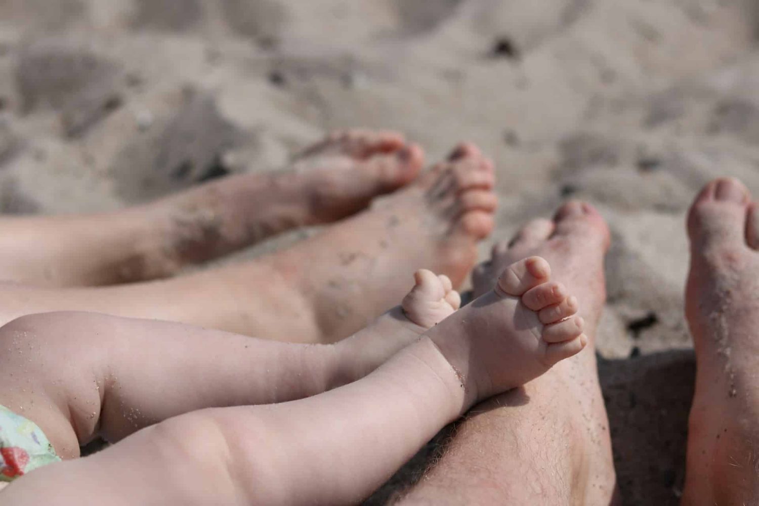 Baby toes and parent toes, covered in sand on the beach. Baby-friendly Caribbean resorts. 