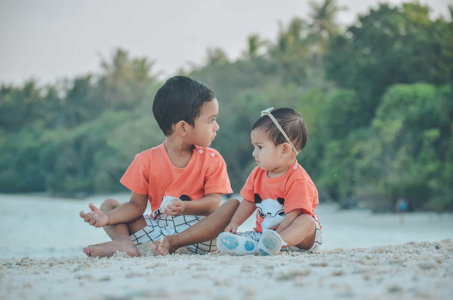 Two siblings in matching outfits sitting on the beach. Baby-friendly Caribbean resorts. 
