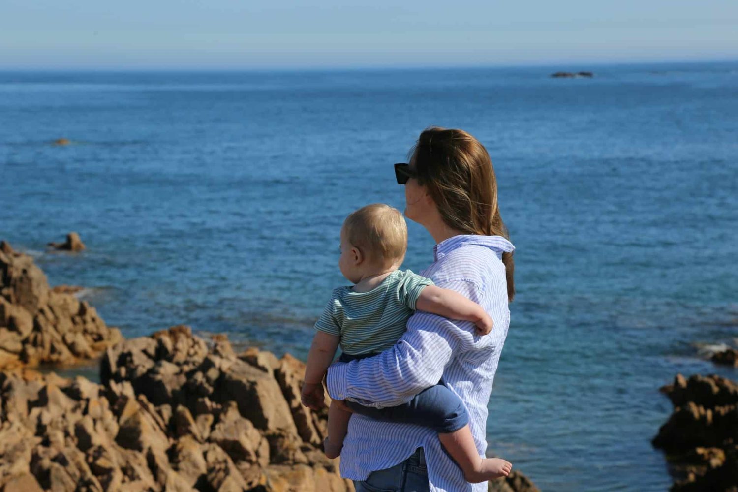 Mom holding infant, looking at the ocean on a hike. Baby-friendly Caribbean resorts. 
