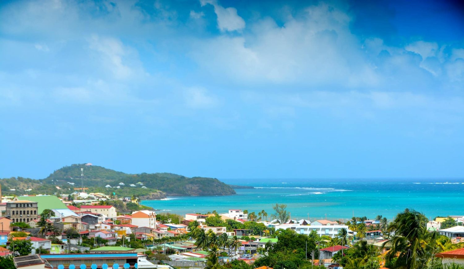 Coastline in Martinique, showing Caribbean Sea and a colorful coastal town. Cheap beach trips.