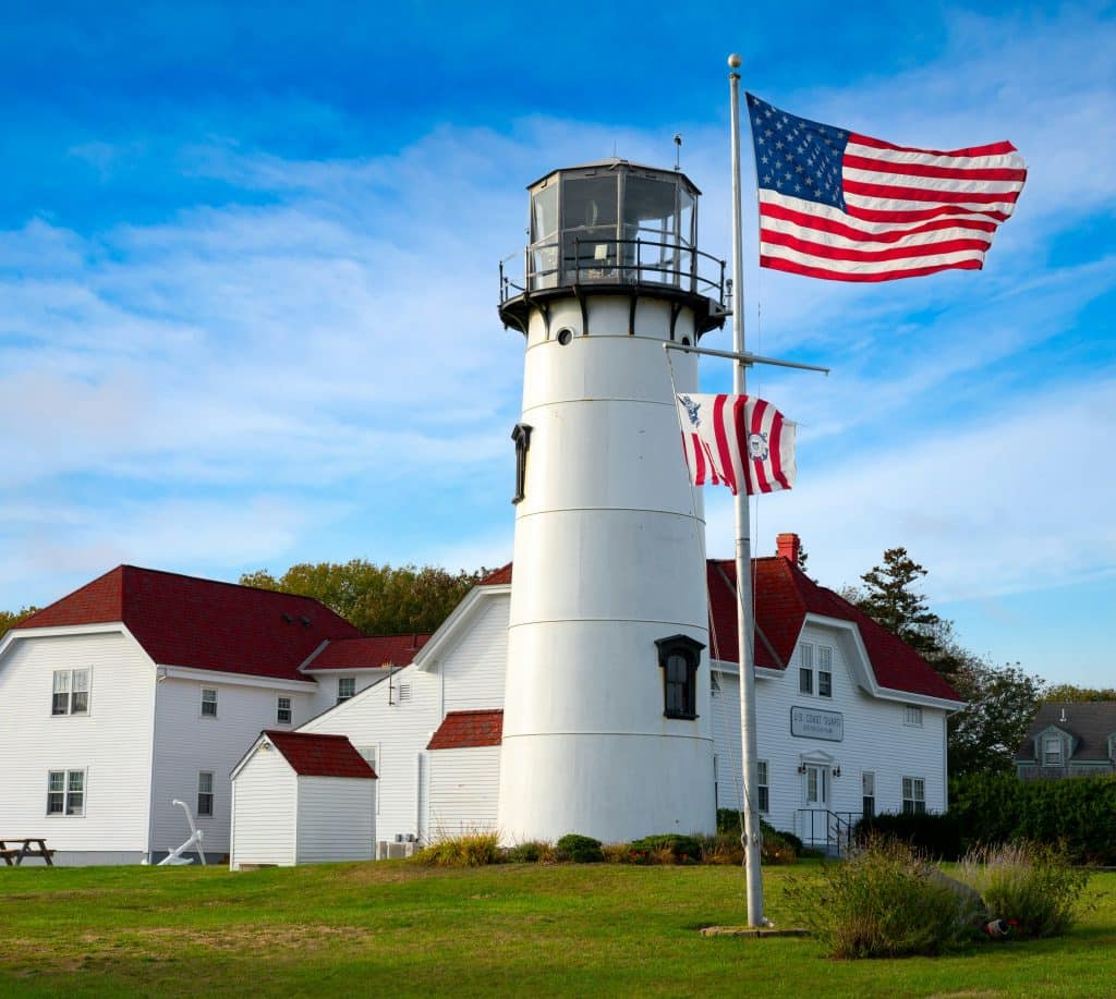 Historic white lighthouse with an American flag in front. 