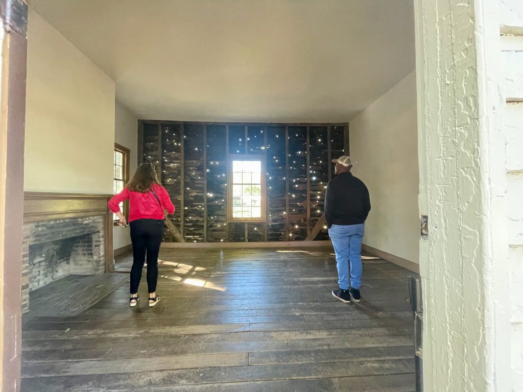 Two people standing in front of wall with bullet holes covering it.