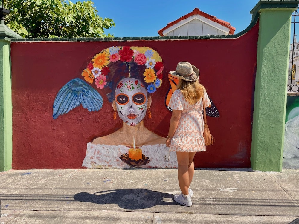 woman standing before a catarina painting on wall