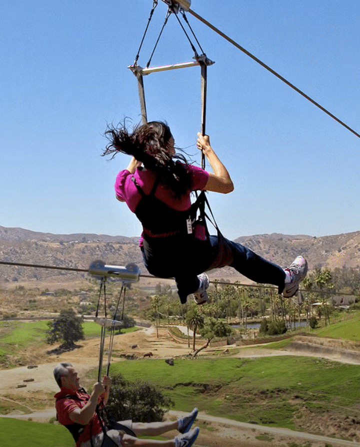 woman ziplining over grassy fields