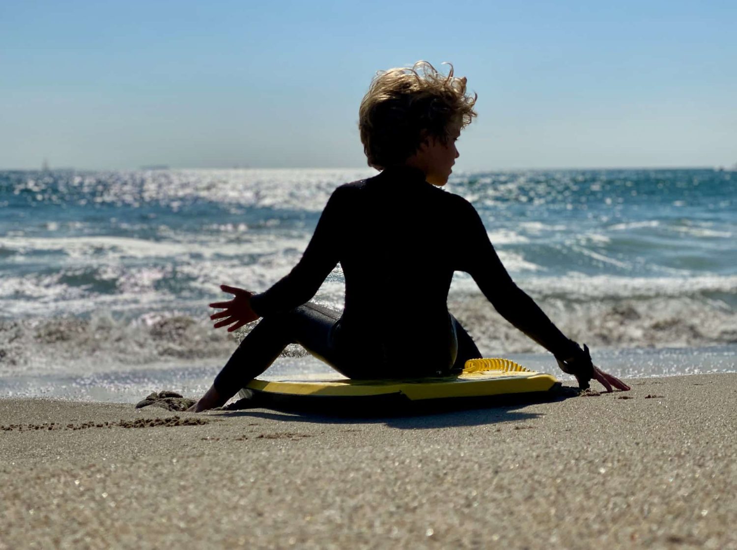 Kid sitting in boogie board on beach. Best beaches in Orange County, CA.