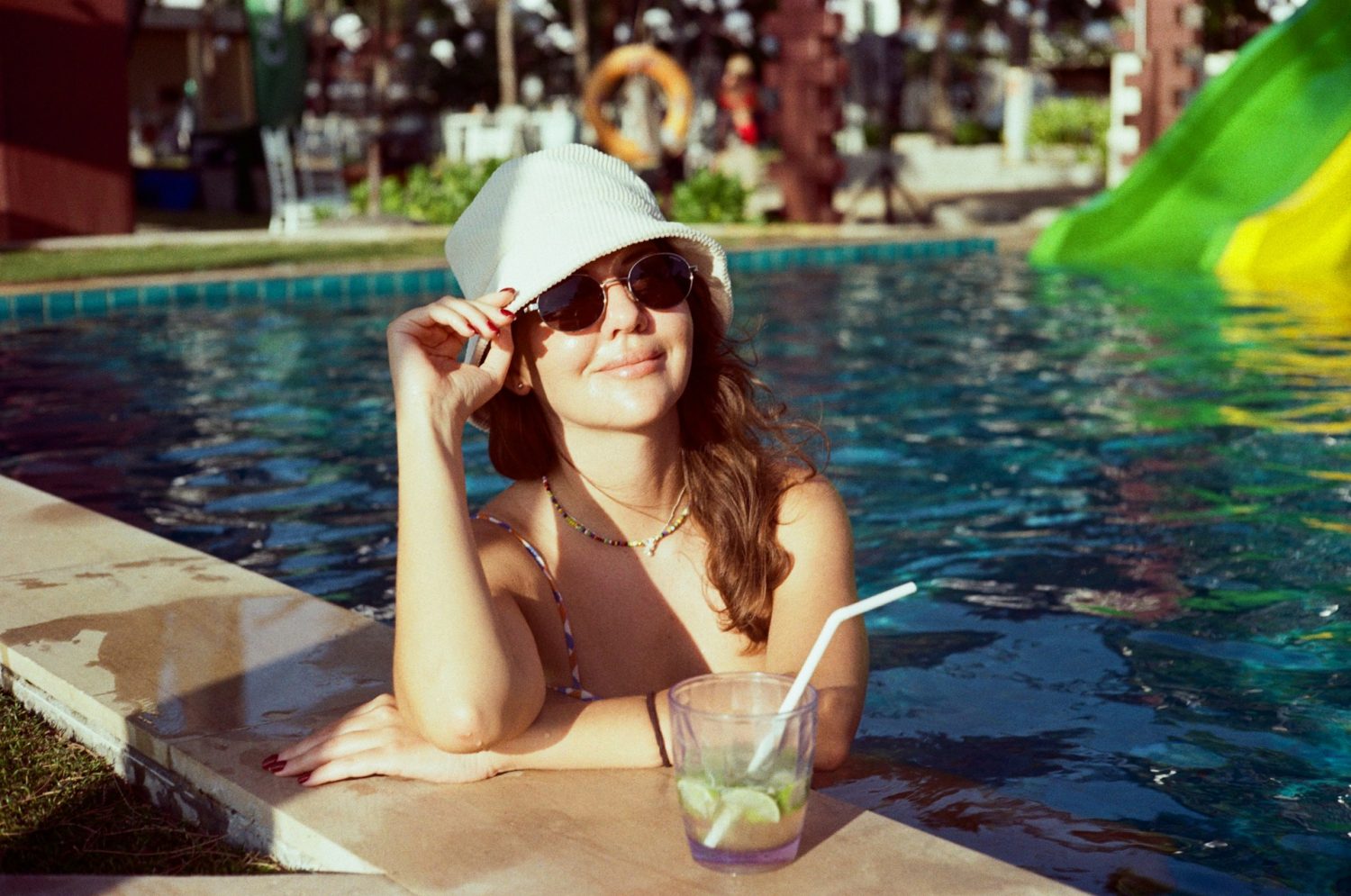 Woman relaxing in the pool, enjoying a cocktail with water slides in the background. All-inclusive kid-friendly resorts in Florida. 
