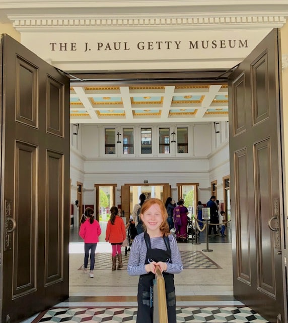 Young girl exploring the J. Paul Getty Museum in Los Angeles, standing among sculptures and art displays just at the door and inside are the museum’s elegant galleries.