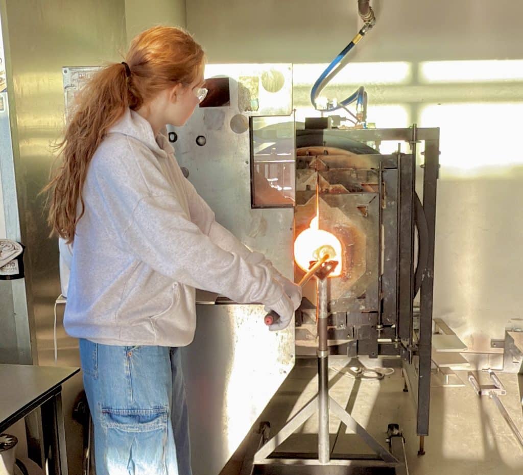 Girl blowing glass at Barrio Glassworks; putting hot glass into kiln.