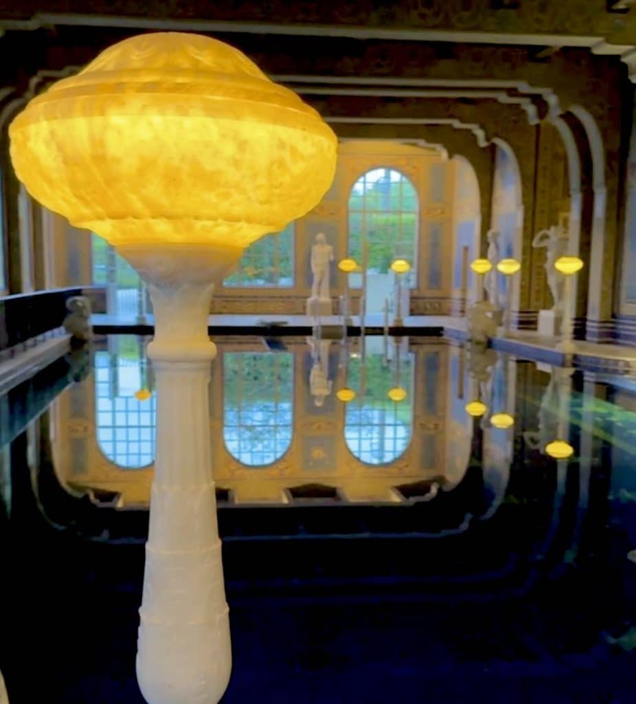Luxurious indoor pool at Hearst Castle, surrounded by ornate architecture, large windows, and intricate tile work, reflecting the estate’s over-the-top design and opulence