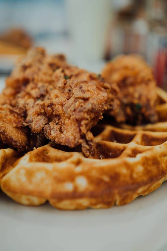 Plate of golden fried chicken served on top of fluffy waffles, drizzled with syrup and garnished with butter, ready to eat.