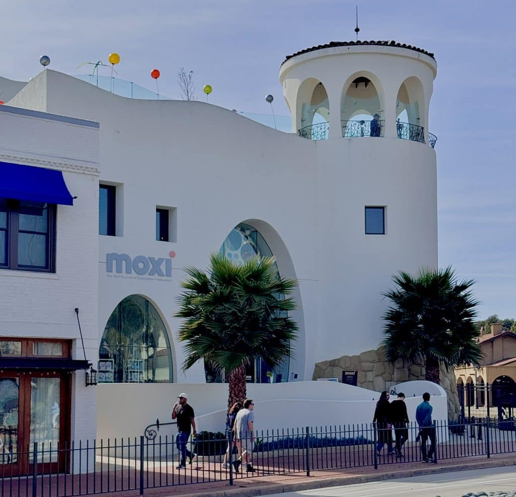Exterior view of MOXI, the Wolf Museum of Exploration + Innovation, a modern building with large windows and playful architectural design, home to interactive science and creativity exhibits for kids and teens