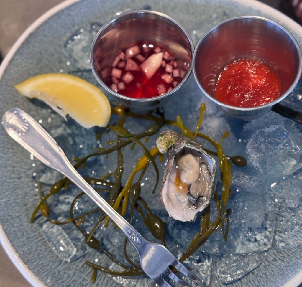 Table at Moby Dick’s Oyster Bar with plates of fresh oysters and coastal dishes, overlooking a panoramic view of the harbor.