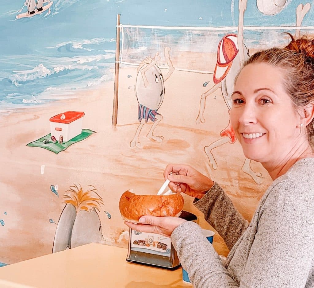 Woman enjoying a bowl of creamy clam chowder at Splash Café in Pismo Beach, with the casual seaside café setting in the background.