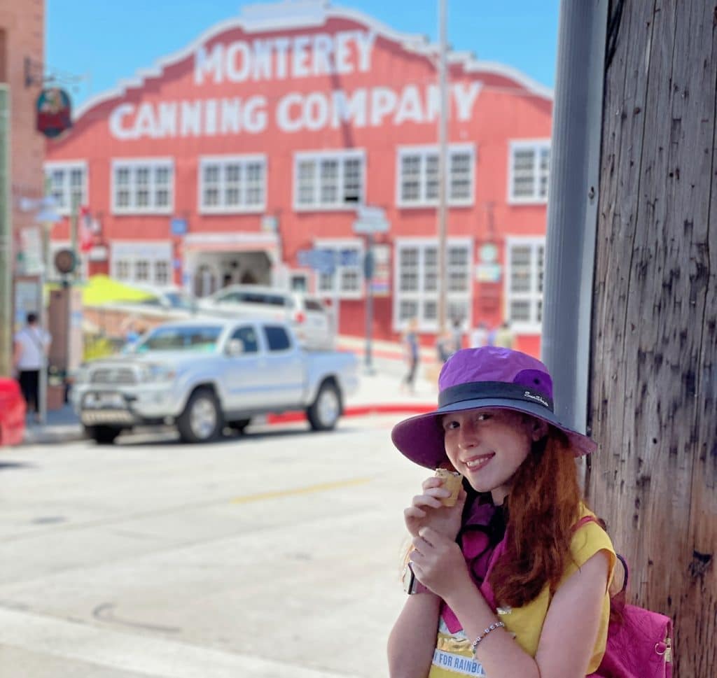 Girl enjoying an ice cream cone outside on Cannery Row in Monterey, with historic buildings and a sunny coastal atmosphere around her.