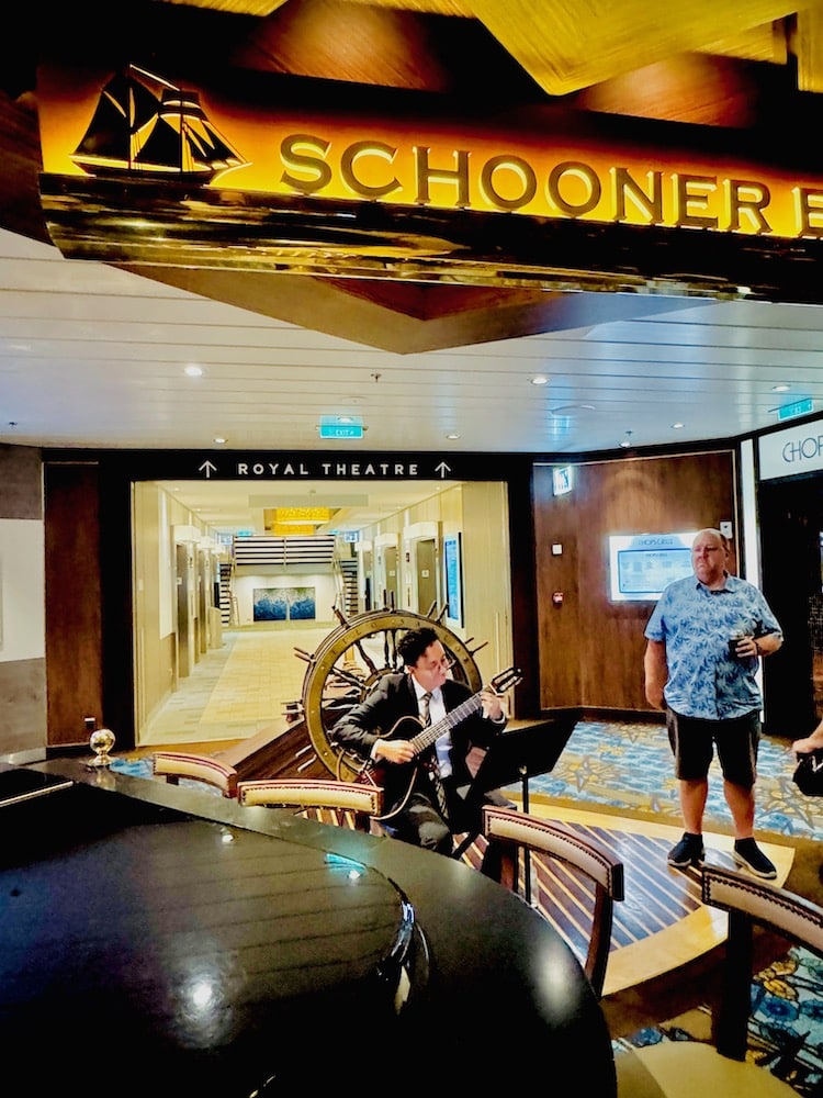 Man playing guitar while a passenger watches at Schooners.