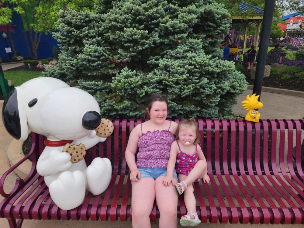 Kings Island With Kids: A Real Parent’s Guide Girls on bench with Snoopy Statue