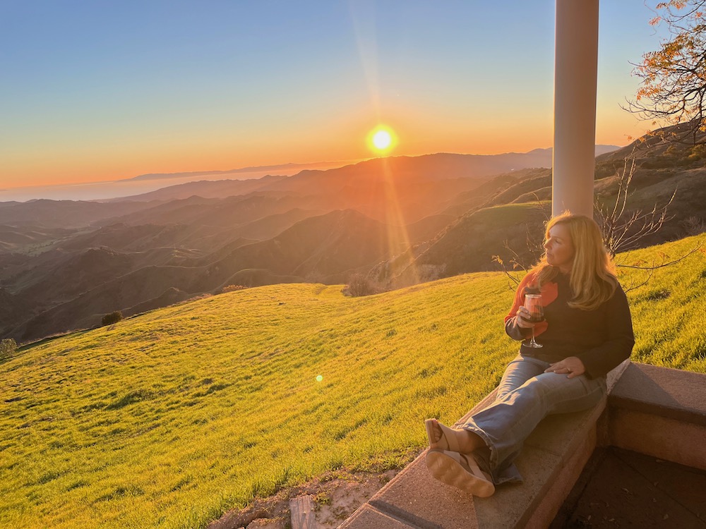 woman sitting on low wall at sunset