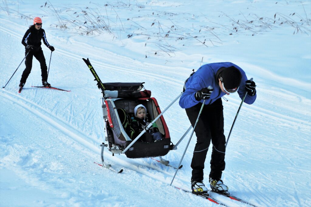 Nordic skiers on a track pulling a baby in a stroller.