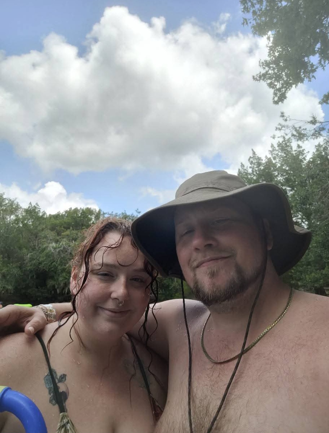 Man and woman smiling with treeline and Florida sky in the background. Hot springs in Florida. 