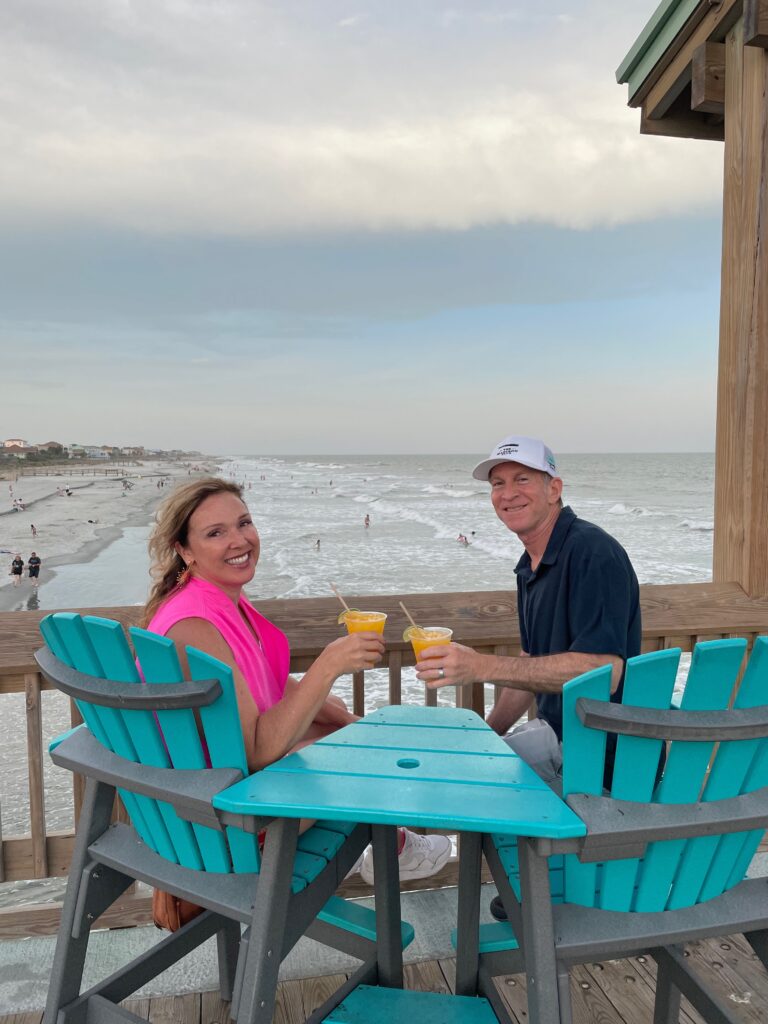 a couple sitting in blue adirondack type chairs on the pier.