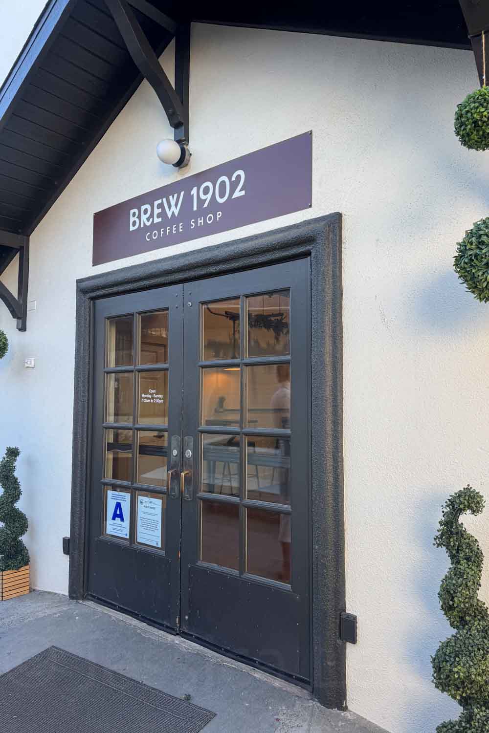 Black double doors mark the entrance to Brew 1902 Coffee Shop. The sign above the door reads “BREW 1902 COFFEE SHOP.”