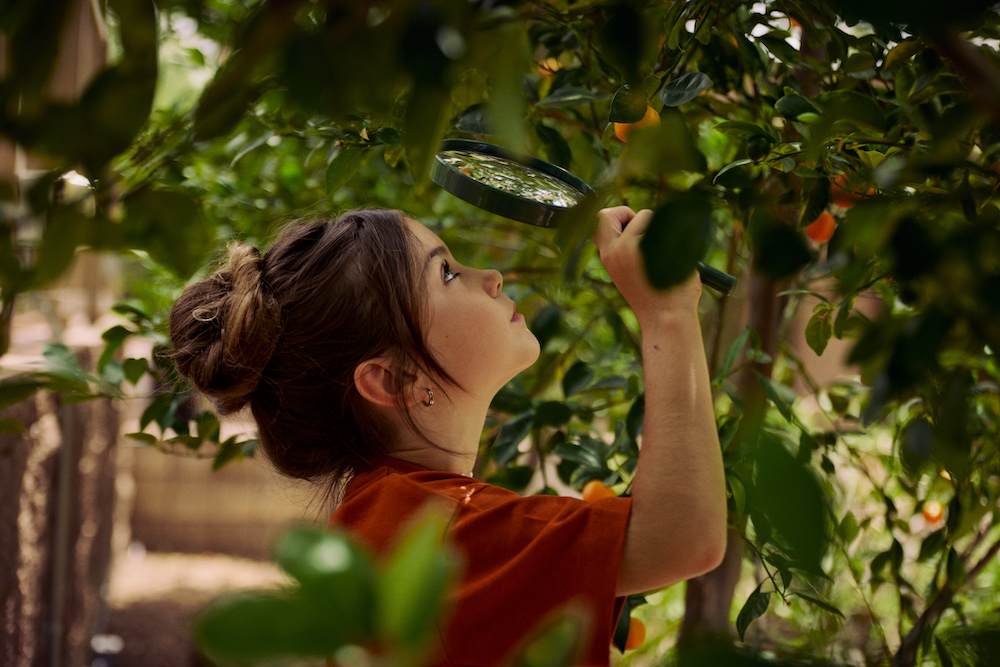 girl looking through magnifying glass at tree