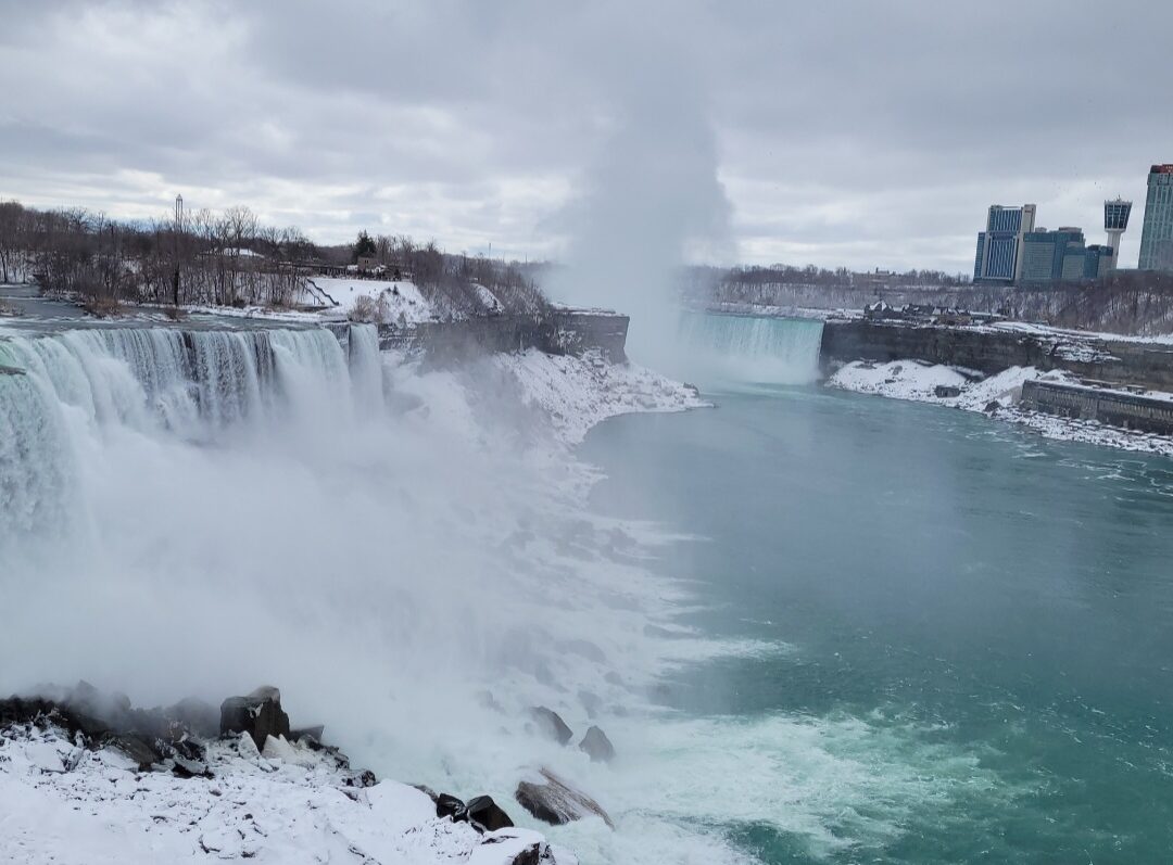 Partially frozen Niagara Falls in winter with mist rising from the gorge Niagara Falls: Which Side is Better?