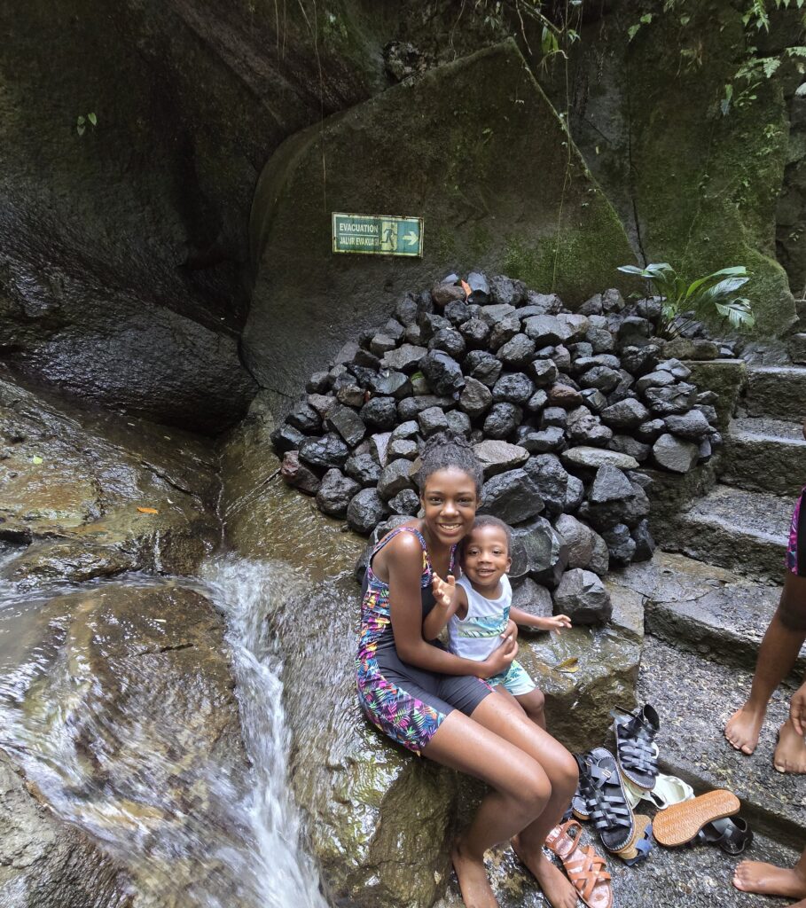 A young girl and boy in front of a small waterfall 